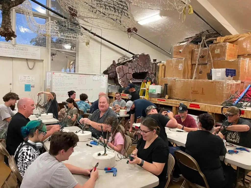 泰勒一家的成员在仓库里帮忙在圆形白色花坛里种植微型树木,为梅萨圣殿圣诞彩灯装饰。