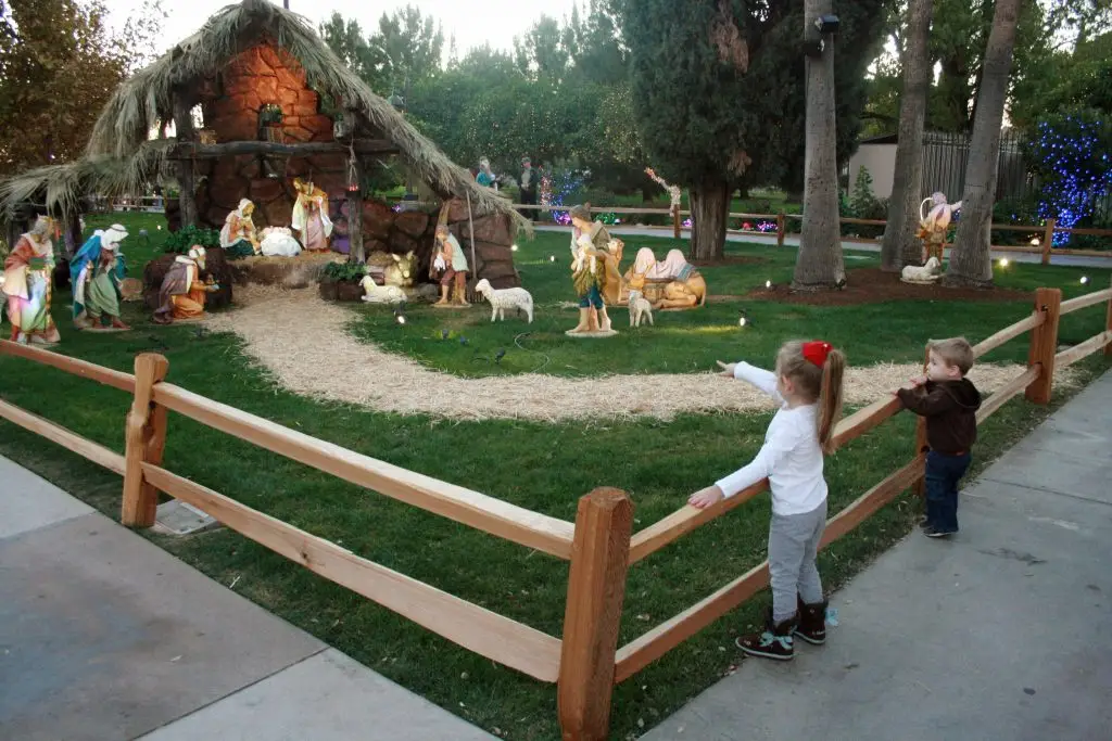 两个孩子在梅萨圣殿观看耶稣诞生的场景。圣诞彩灯装饰着背景中的灌木丛。