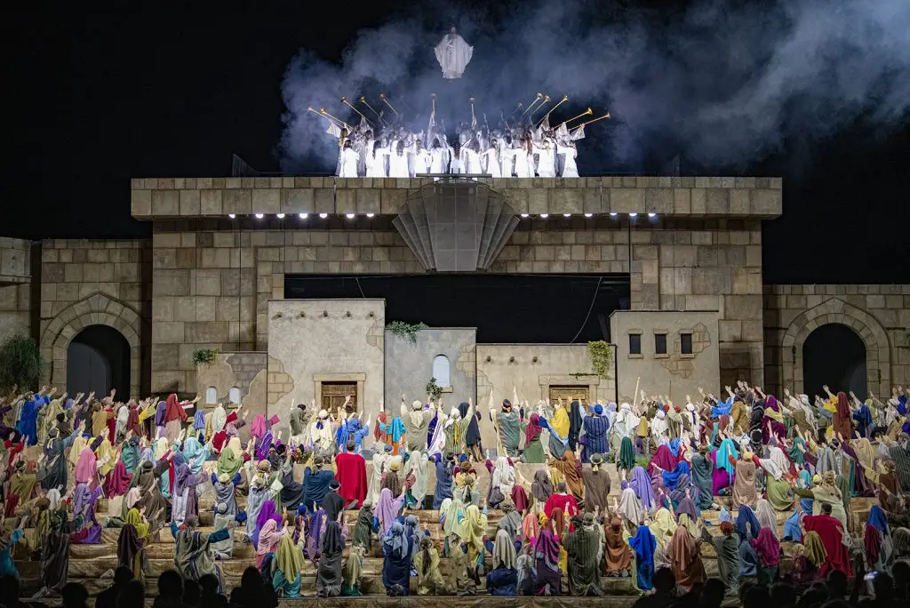 在梅萨圣殿复活节盛会的户外舞台上,复活的救世主胜利地站在吹着号角的天使之上。下面是一群穿着戏服的兴奋的演员跪下并举起双臂指向基督。